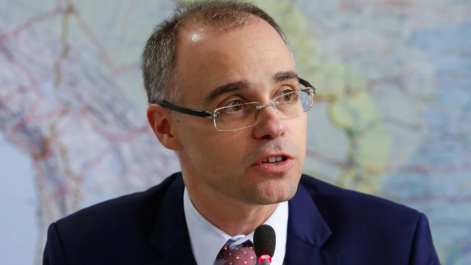 Ministro André Mendonça fala ao microfone em entrevista, de óculos e terno azul