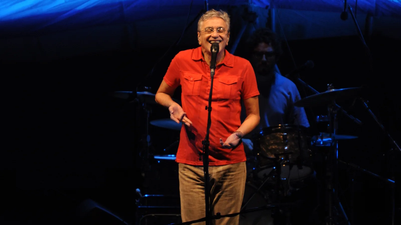 Caetano Veloso cantando sozinho no palco, com banda ao fundo