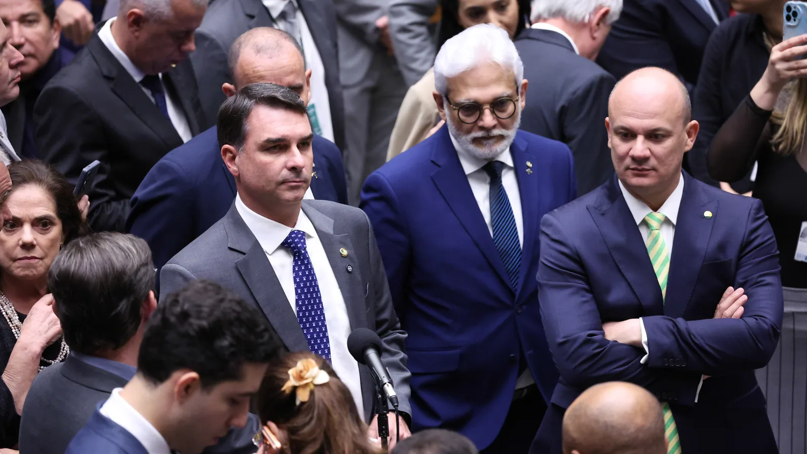Flávio Bolsonaro em sessão do Congresso, ao microfone, cercado por parlamentares
