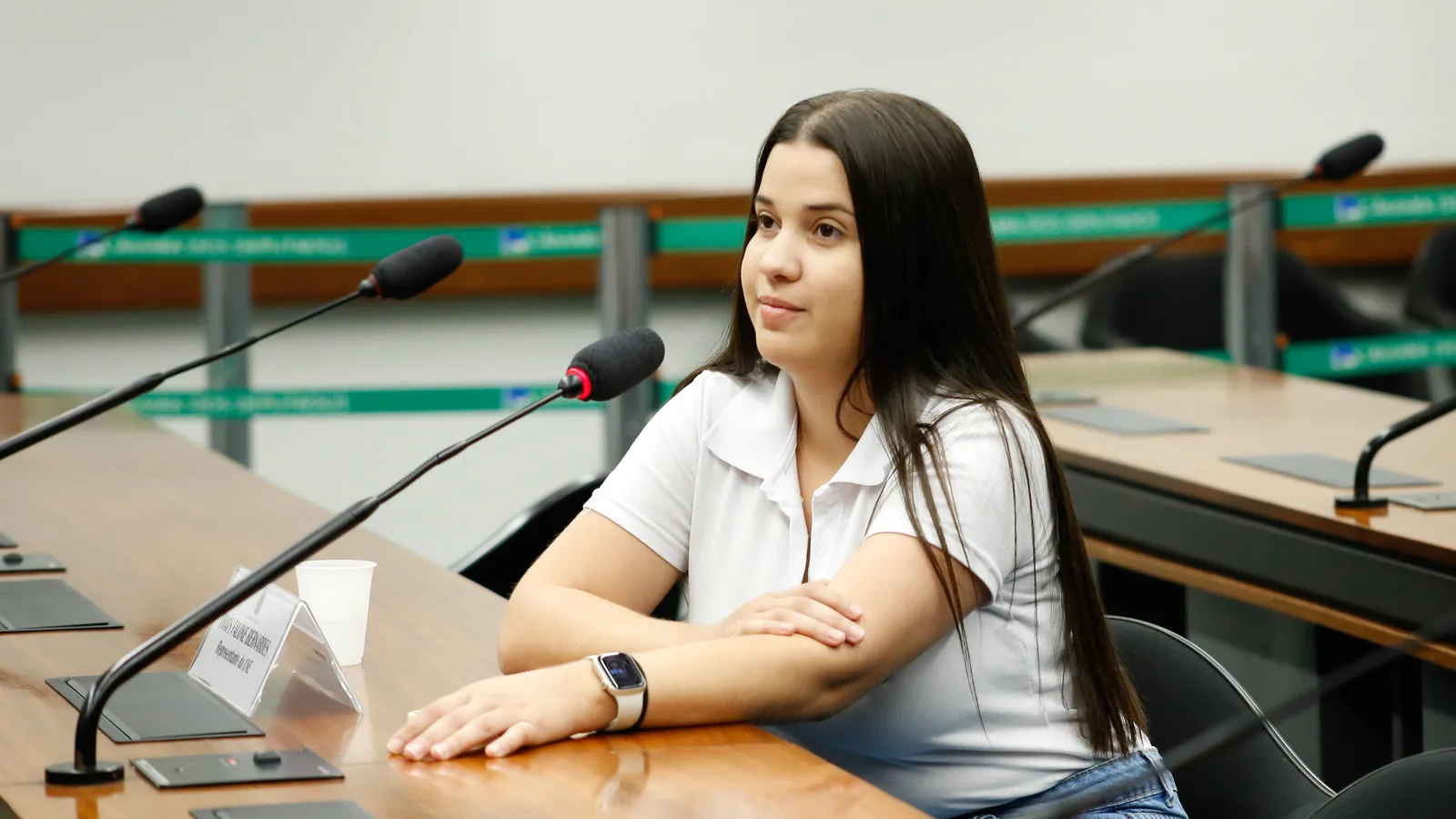 Jovem eleitora participa de audiência pública sobre engajamento no processo eleitoral, sentada à mesa com microfone
