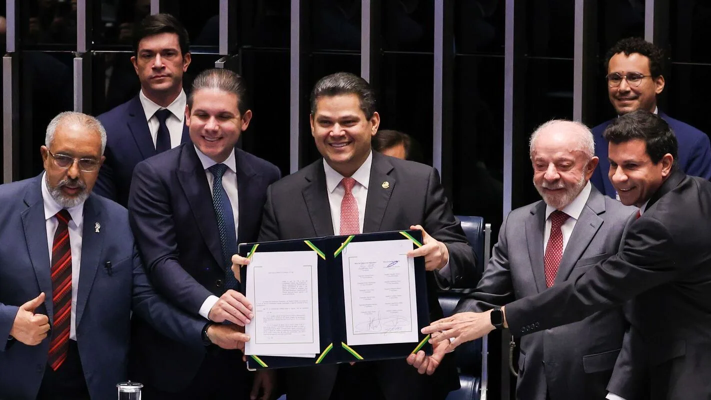 Lula ao lado de Hugo Motta e outras autoridades segurando documento assinado em cerimônia no Congresso
