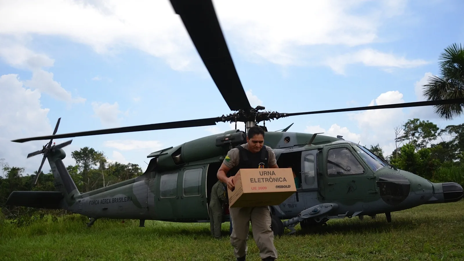 Militar carrega caixa com urna eletrônica próximo a helicóptero durante apoio logístico a eleições