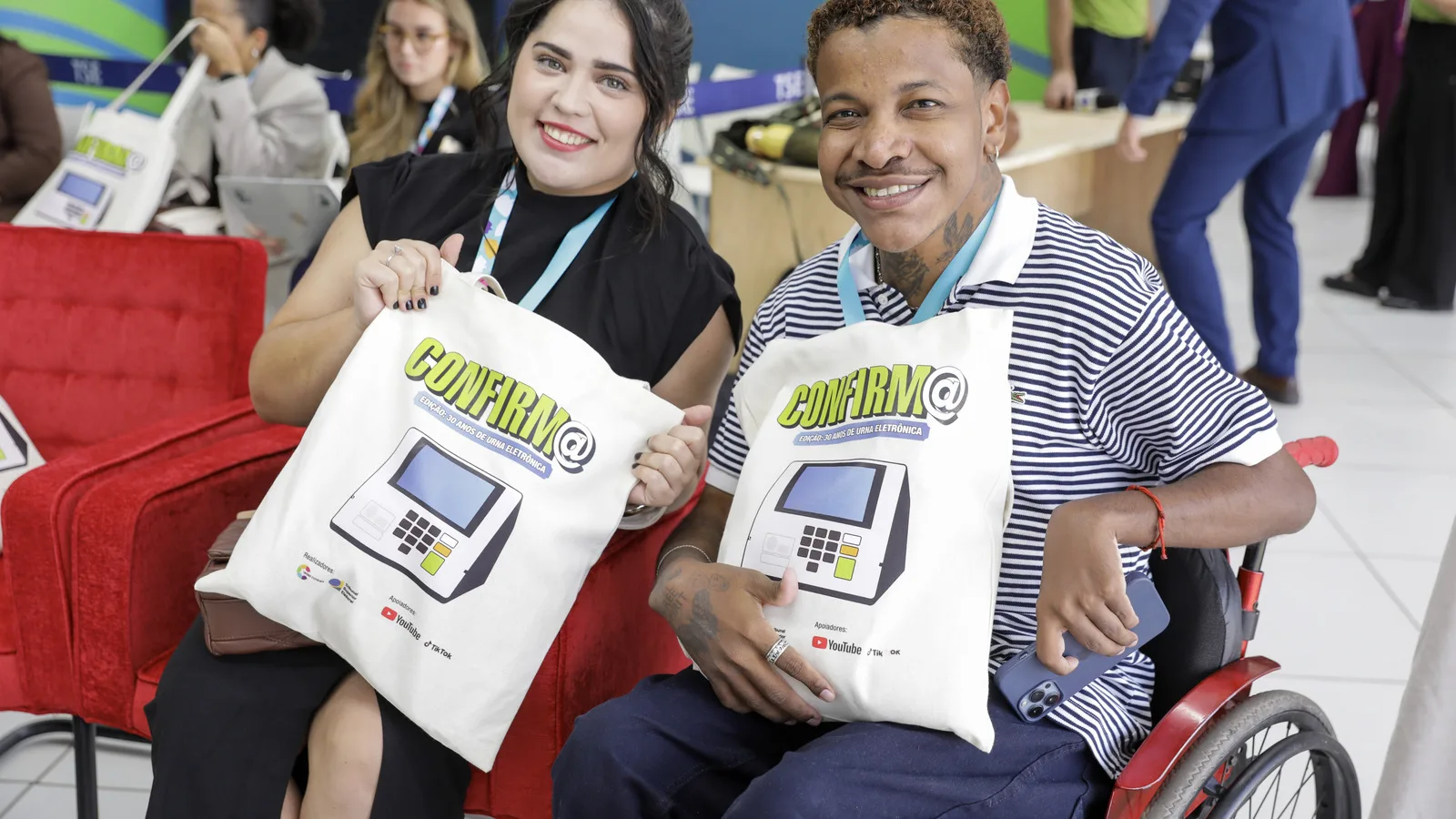 Mesa de evento do TSE com participantes segurando sacolas da campanha Confirm@ contra desinformação