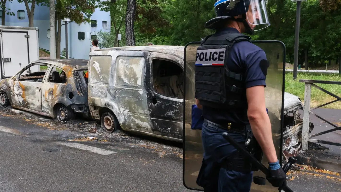 Policial ao lado de veículos incendiados durante protesto