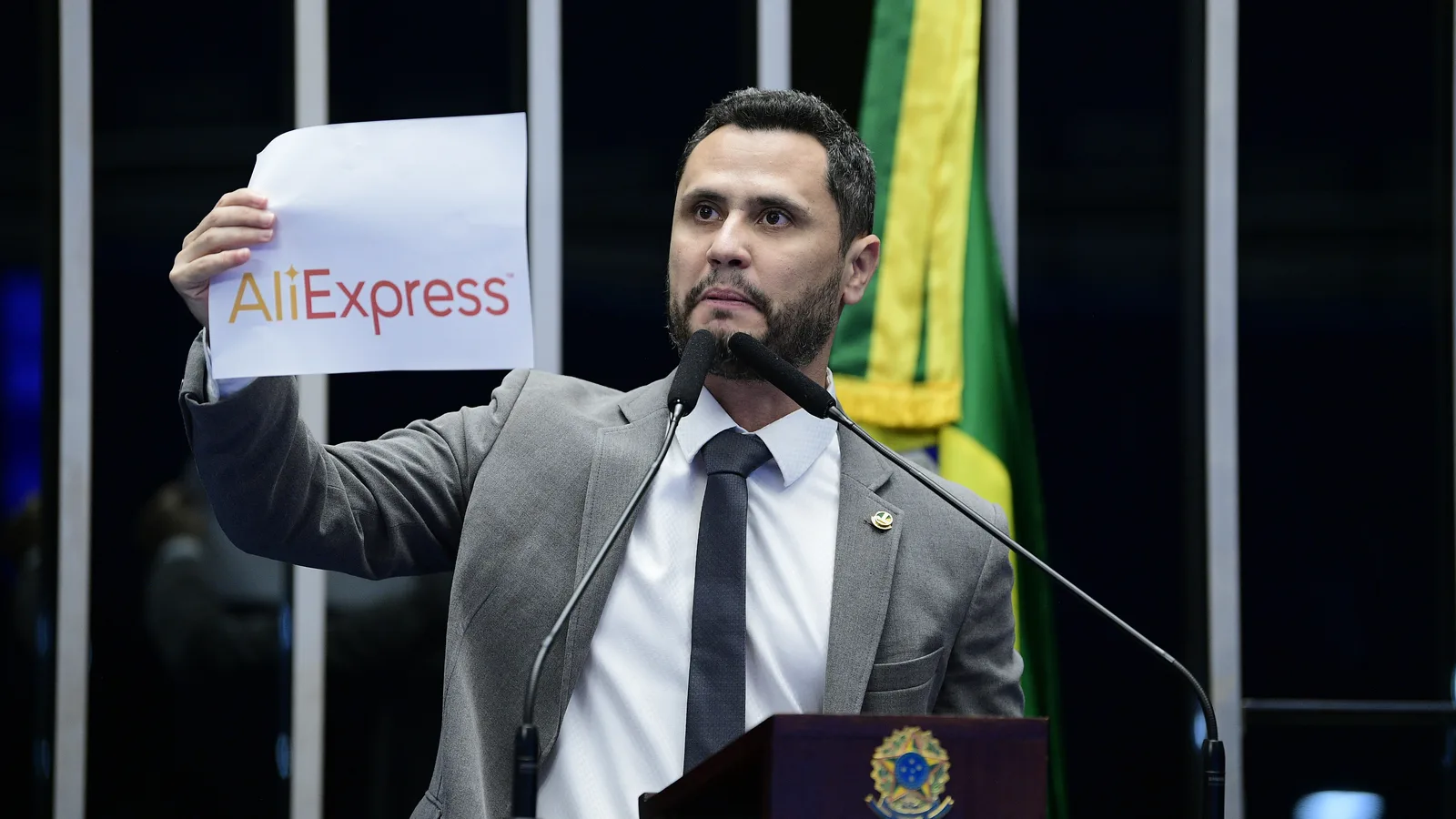 Homem discursa em plenário segurando um cartaz
