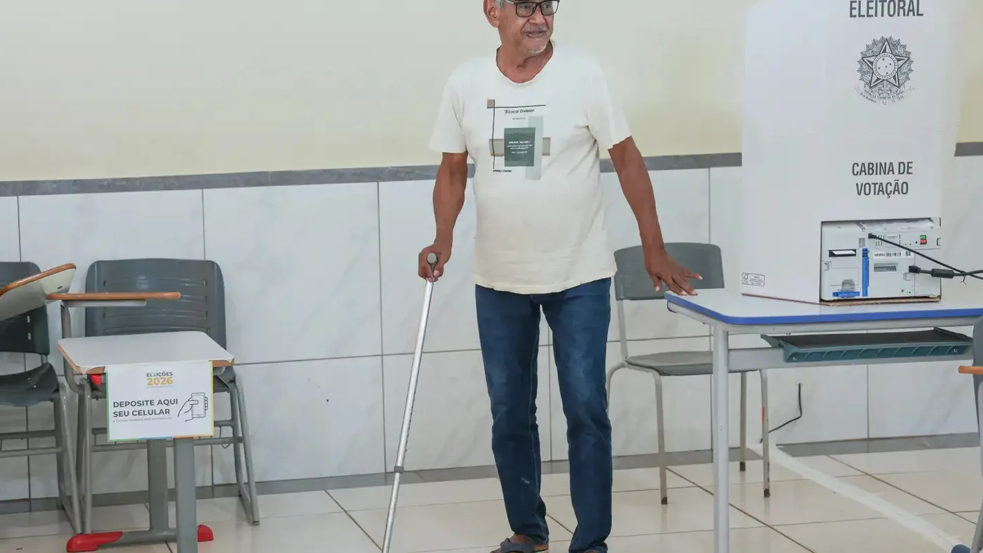 Eleitor idoso em cabine de votação, segurando uma bengala, em seção eleitoral