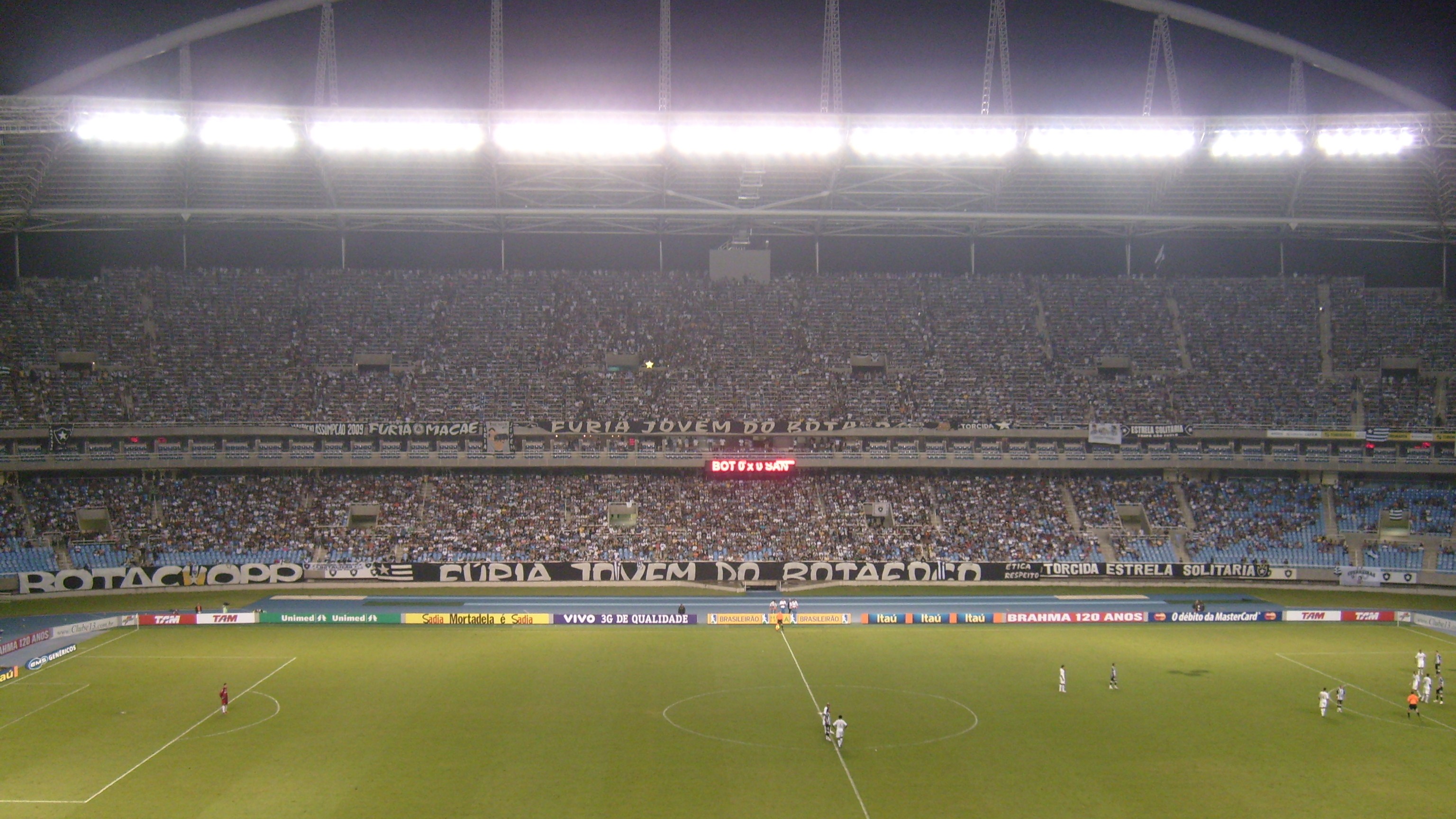 Estádio Nilton Santos lotado durante partida do Botafogo à noite, com faixas da torcida (foto de arquivo)