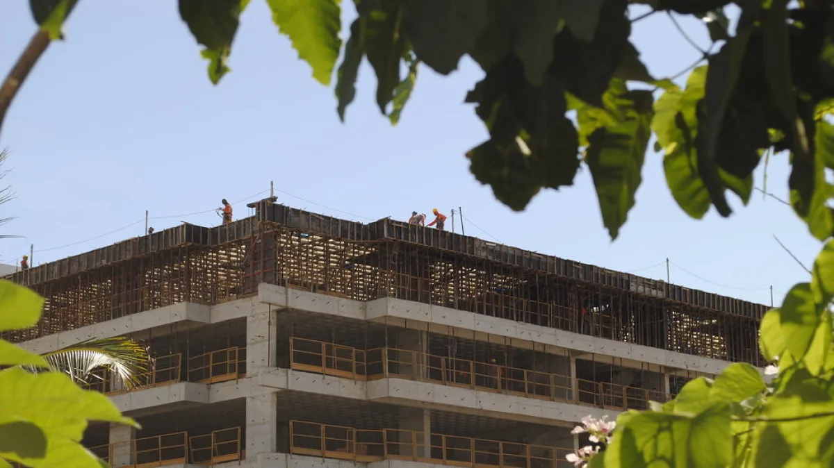 Trabalhadores em obra de prédio em construção, com estrutura de concreto e ferragens aparentes